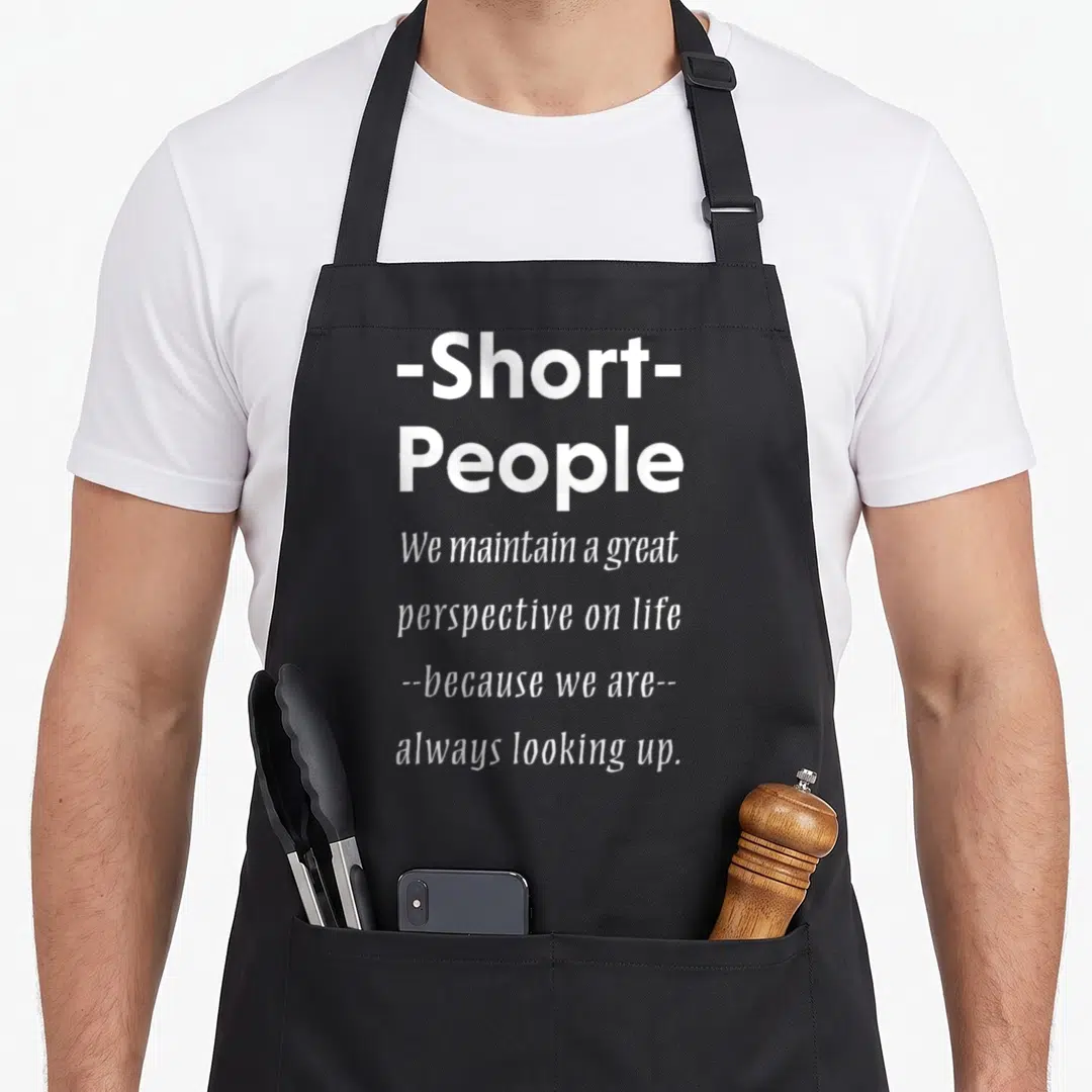 Irony sarcasm apron - White stacked text reading -Short- People We maintain a great perspective on life always looking — shown on a black cotton canvas apron against a white background