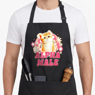 Cat alpha apron - Orange cartoon kitten with pink circle and ALPHA MALE text surrounded by flowers — shown on a black cotton canvas apron against a white background