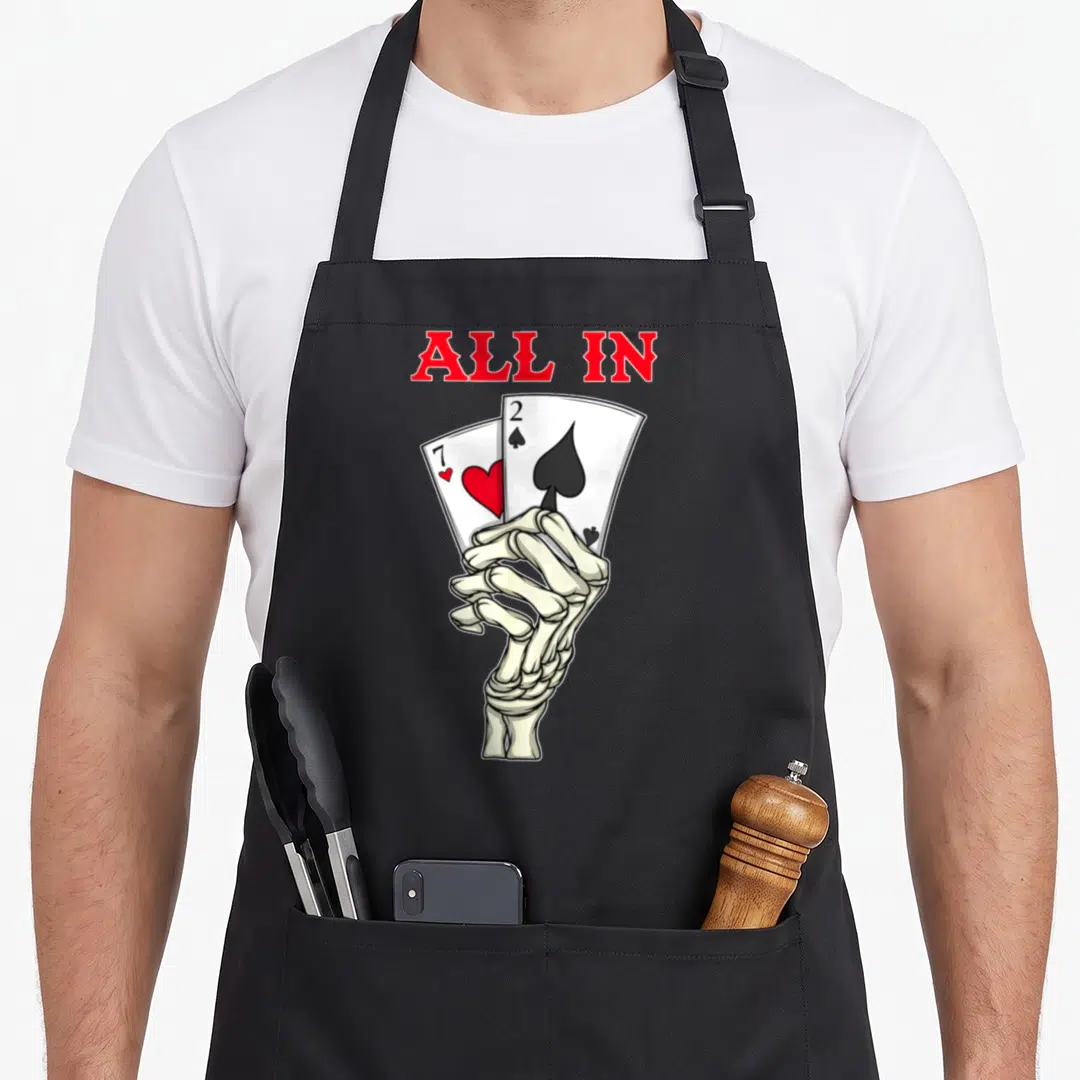 Poker skeleton apron - Skeleton hand holding 7 of hearts and 2 of spades below red ALL IN text — shown on a black cotton canvas apron against a white background