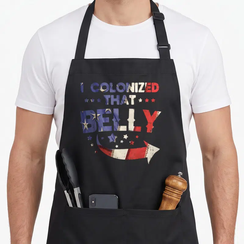 Colonized 4th of july apron - I COLONIZED THAT BELLY text in red white blue with stars and curved arrow — shown on a black cotton canvas apron against a white background
