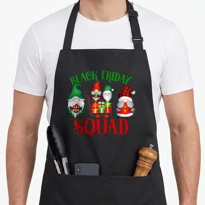 Gnome black friday apron - Four cartoon gnomes with shopping cart and presents under arched text — shown on a black cotton canvas apron against a white background