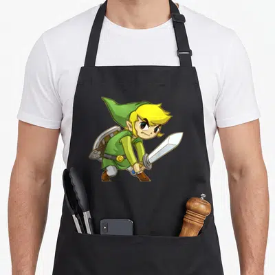 Link track apron - Cartoon elf with yellow hair holding silver sword, green tunic, brown boots, shield on back — shown on a black cotton canvas apron against a white background