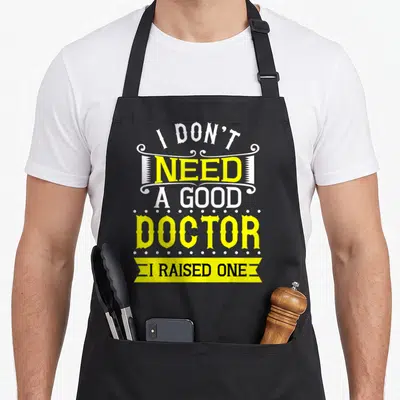 Medical doctor with apron - I don't need a good doctor I raised one text art in yellow and white — shown on a black cotton canvas apron against a white background