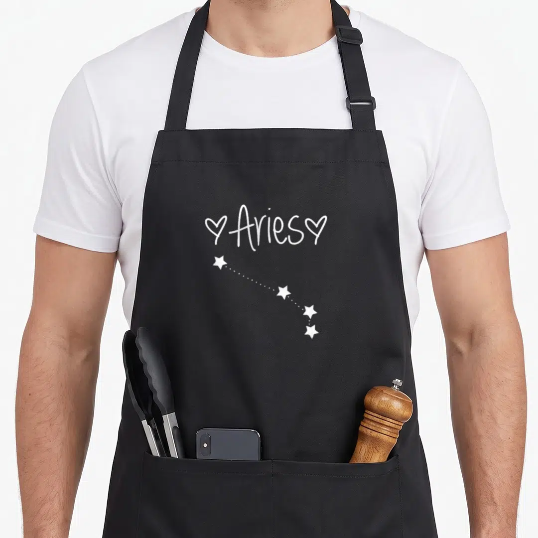 Horoscope birthday apron - White Aries text with two hearts and four stars connected by dotted line — shown on a black cotton canvas apron against a white background
