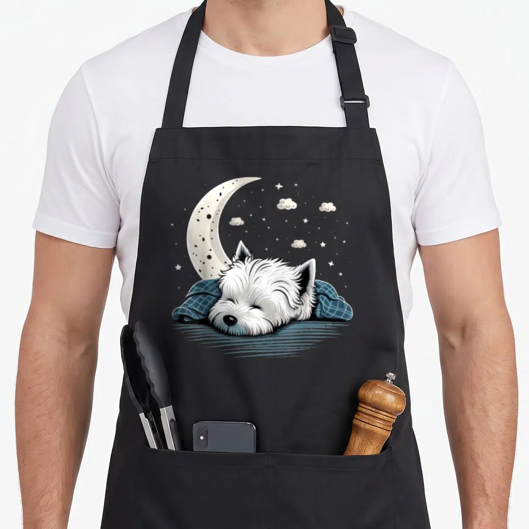Napping westie apron - Sleeping white dog under blue blanket with crescent moon and stars cartoon art — shown on a black cotton canvas apron against a white background