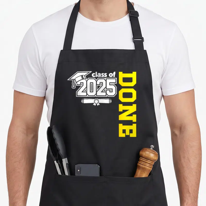 Grad congrat apron - White graduation cap and diploma with class of 2025 text and vertical yellow DONE lettering — shown on a black cotton canvas apron against a white background