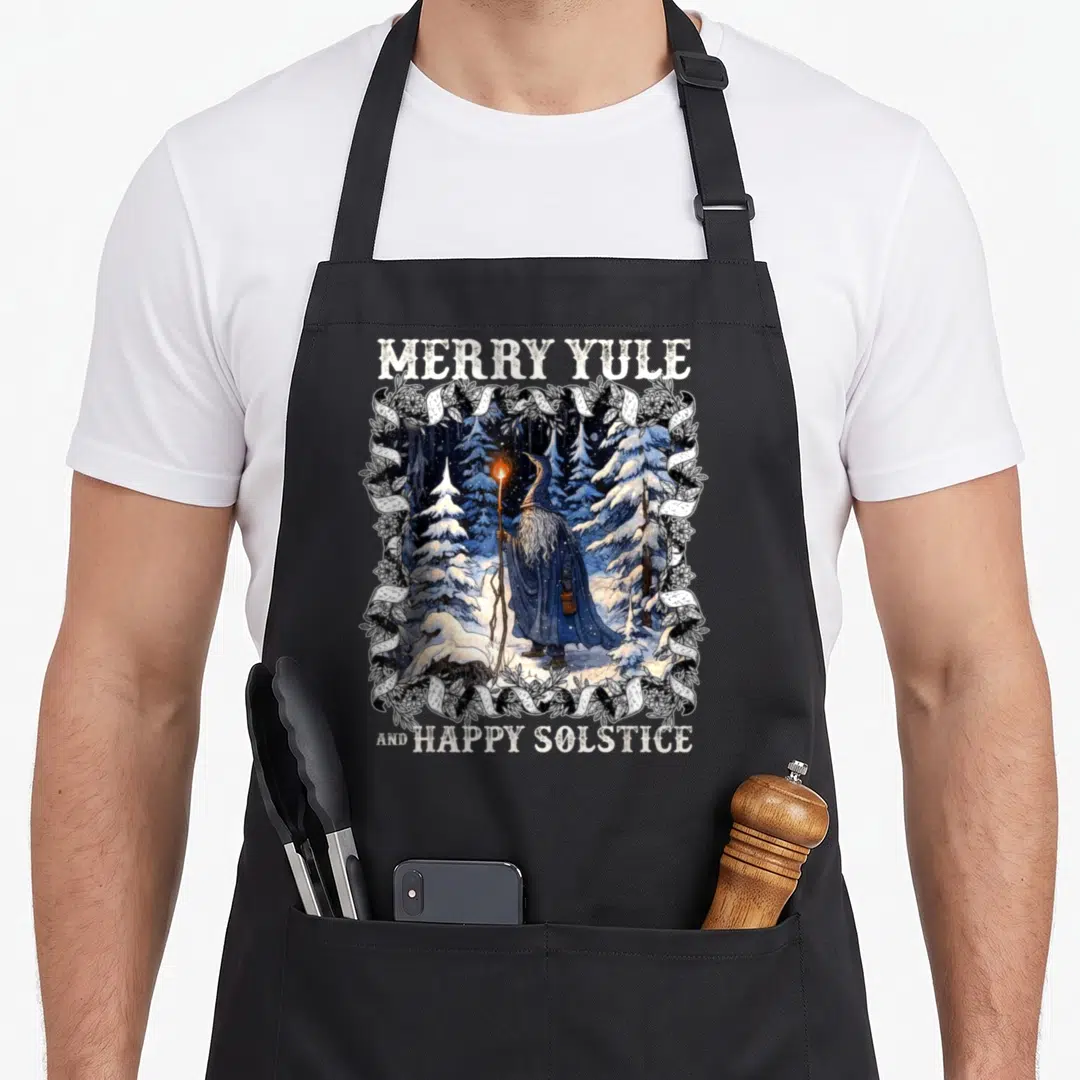 Solstice merry christmas apron - Wizard in snowy forest with Merry Yule and Happy Solstice text framed by ribbons — shown on a black cotton canvas apron against a white background