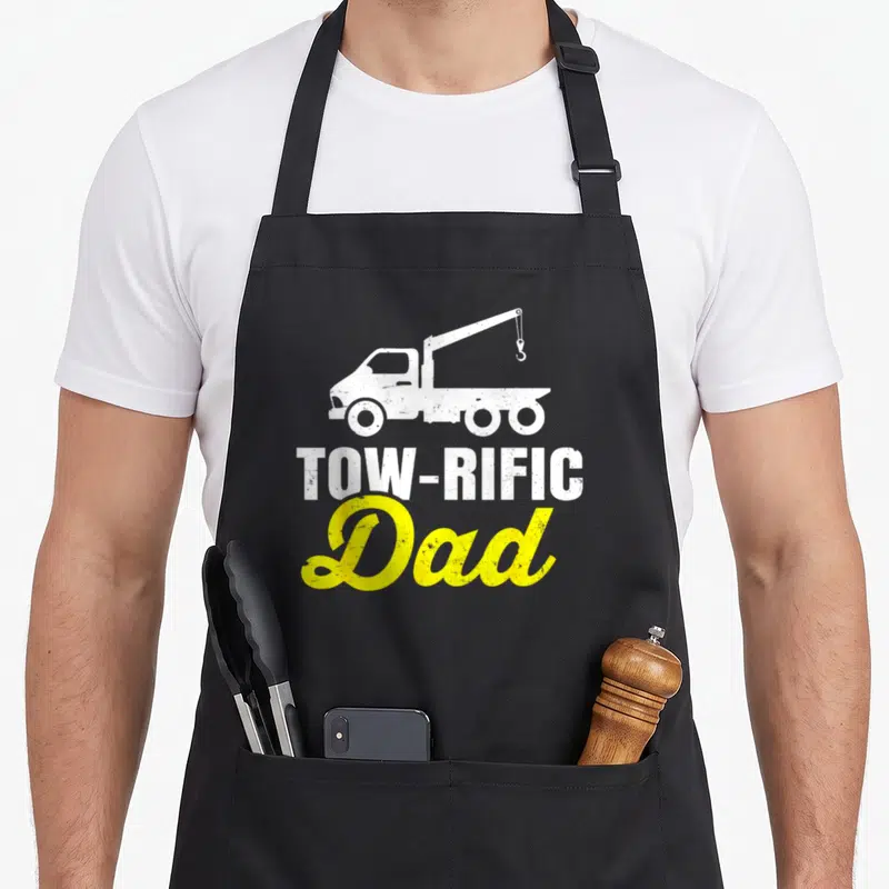 Driver father truck apron - White tow truck above TOW-RIFIC and yellow Dad text in distressed style — shown on a black cotton canvas apron against a white background