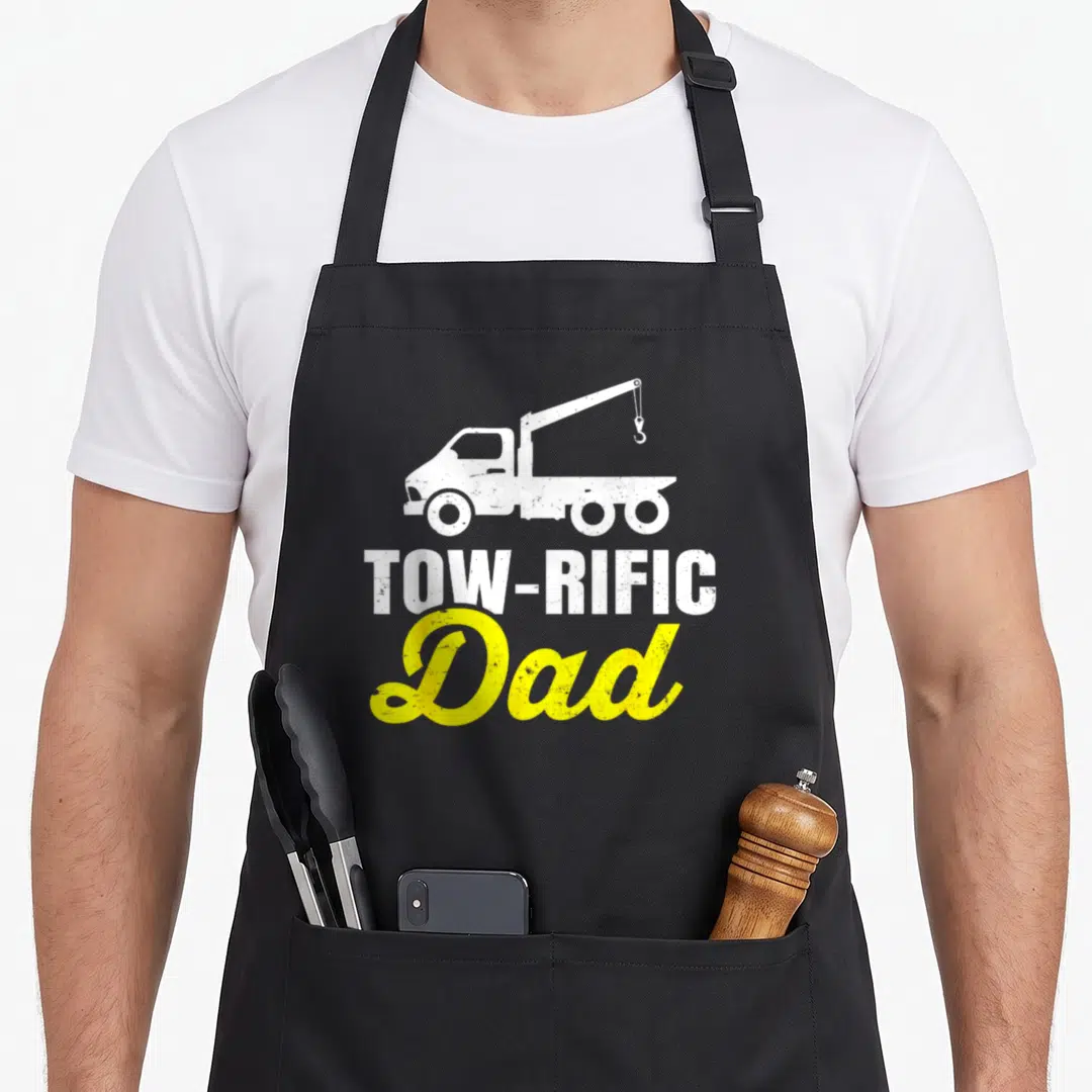 Driver father truck apron - White tow truck above TOW-RIFIC and yellow Dad text in distressed style — shown on a black cotton canvas apron against a white background
