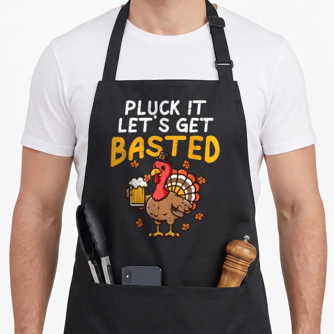 Pluck thanksgiving apron - Cartoon turkey in pilgrim hat holding beer under text Pluck It Lets Get Basted — shown on a black cotton canvas apron against a white background