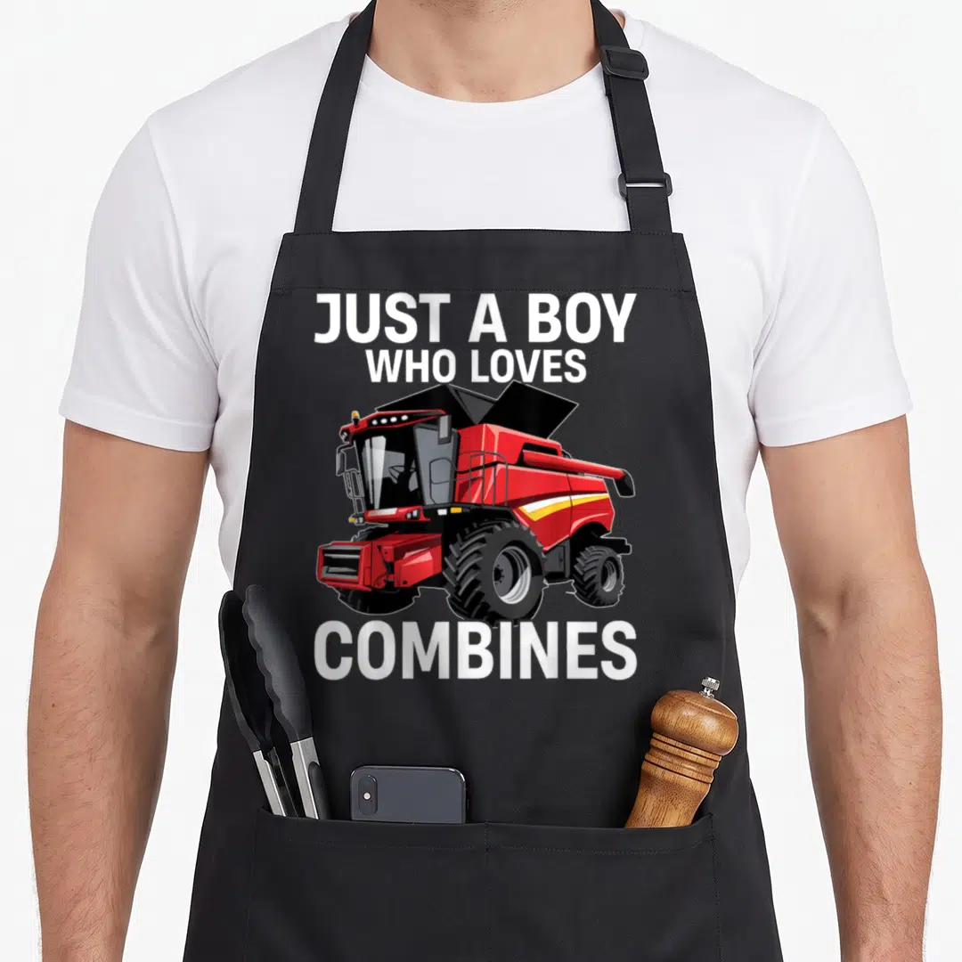 Funny harvester combine apron - Red combine harvester illustration with white text Just a Boy Who Loves Combines — shown on a black cotton canvas apron against a white background