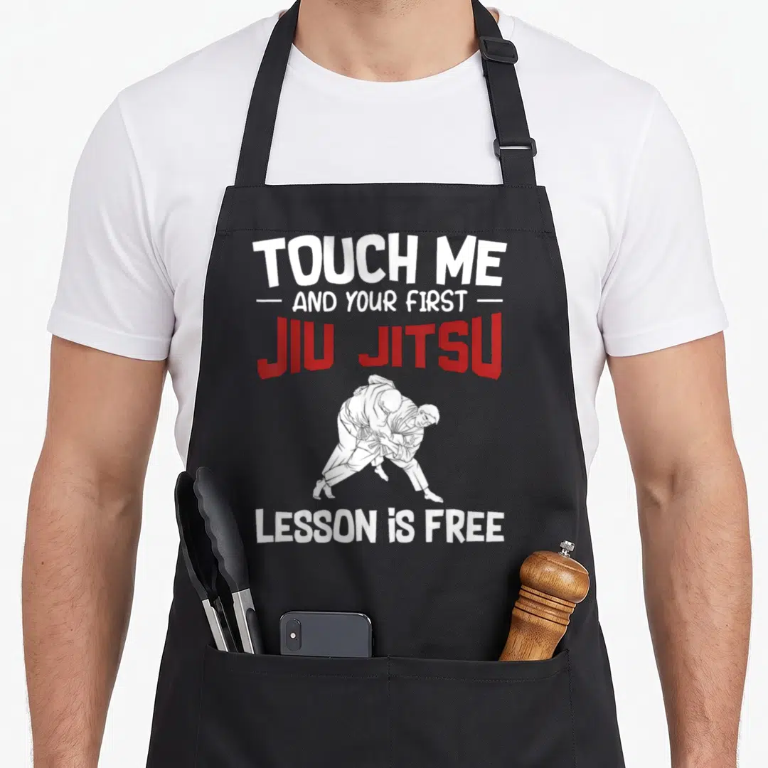 Touch jiu quotes apron - Two fighters grappling in white line art below red and white text reading TOUCH ME AND YOUR — shown on a black cotton canvas apron against a white background