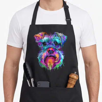 Splash schnauzer apron - Multicolored watercolor dog head with blue pink yellow green purple splatter effects — shown on a black cotton canvas apron against a white background