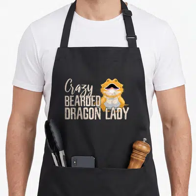 Beardie bearded dragon apron - Cartoon orange lizard beside stacked text reading Crazy BEARDED DRAGON LADY — shown on a black cotton canvas apron against a white background