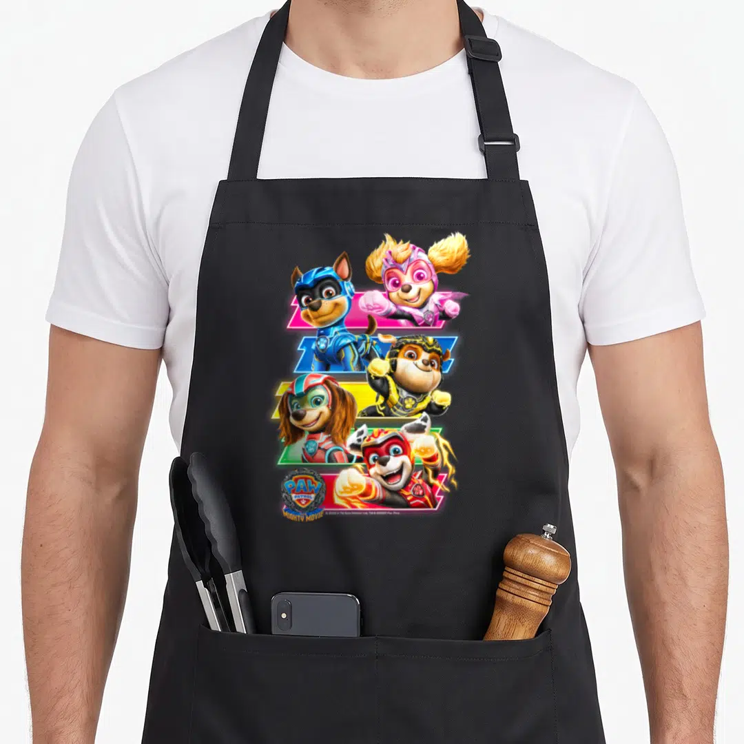Mighty paw apron - Four puppies in superhero suits with PAW PATROL MIGHTY MOVIE text in blue red yellow and pink — shown on a black cotton canvas apron against a white background
