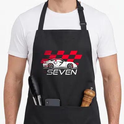 7th car apron - White race car with black 7 and SEVEN text over red grey checkered pattern — shown on a black cotton canvas apron against a white background