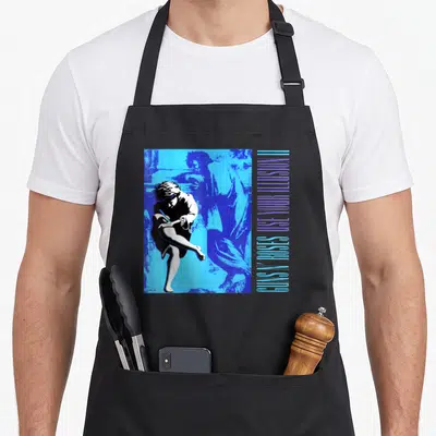 Use rose apron - Two figures in blue and white with vertical Use Your Illusion lettering — shown on a black cotton canvas apron against a white background