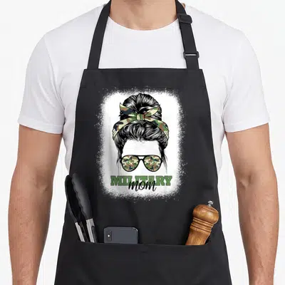Bleached patriotic apron - Stylized woman with camo bun and sunglasses, MILITARY mom text in green and black — shown on a black cotton canvas apron against a white background