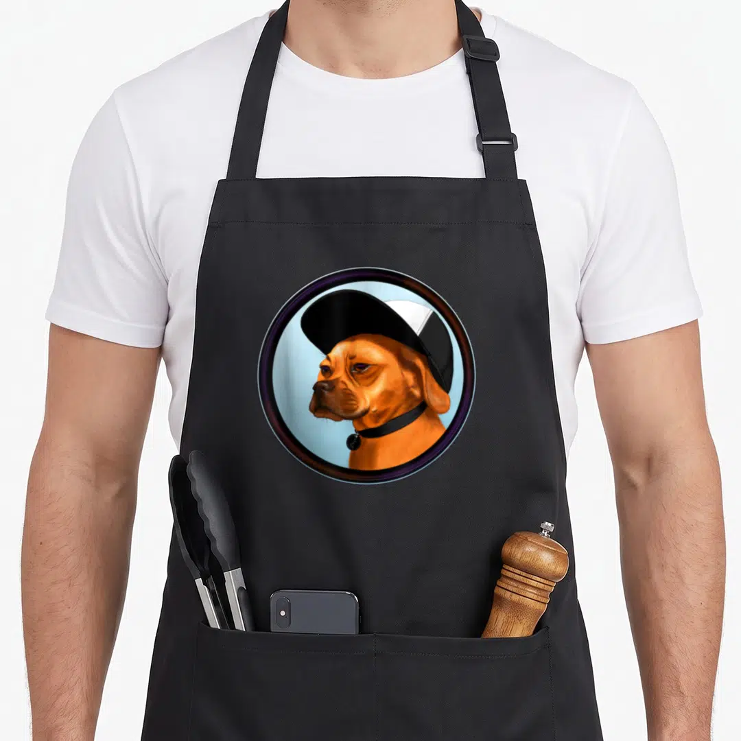 Cute puggle apron - Realistic orange-brown dog wearing black cap and collar inside circular metallic frame on blue — shown on a black cotton canvas apron against a white background