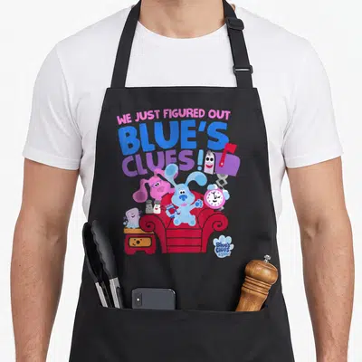 Clue novelty apron - Blue dog in red chair surrounded by characters under stacked text WE JUST FIGURED OUT BLUE'S CLUES! — shown on a black cotton canvas apron against a white background