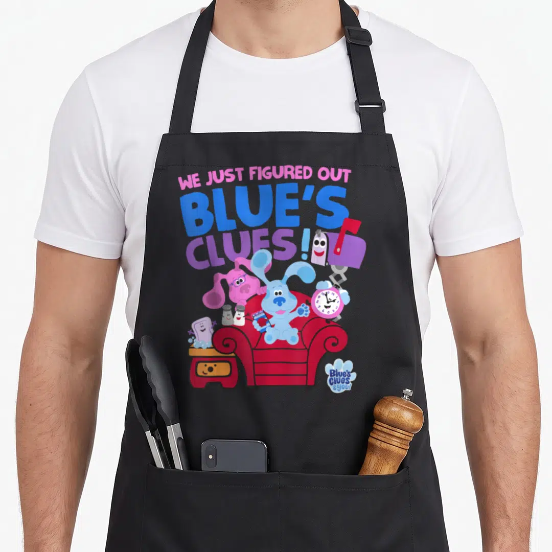Clue novelty apron - Blue dog in red chair surrounded by characters under stacked text WE JUST FIGURED OUT BLUE'S CLUES! — shown on a black cotton canvas apron against a white background