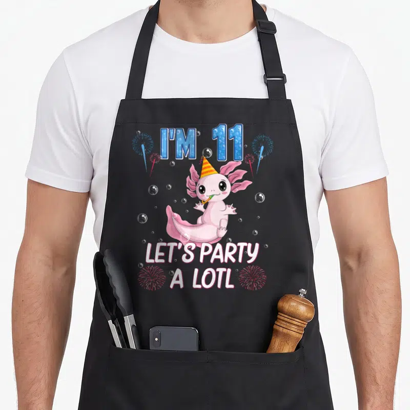 Axolotl 11th birthday apron - Pink axolotl with party hat blowing blower surrounded by blue text I'M 11 and white text — shown on a black cotton canvas apron against a white background