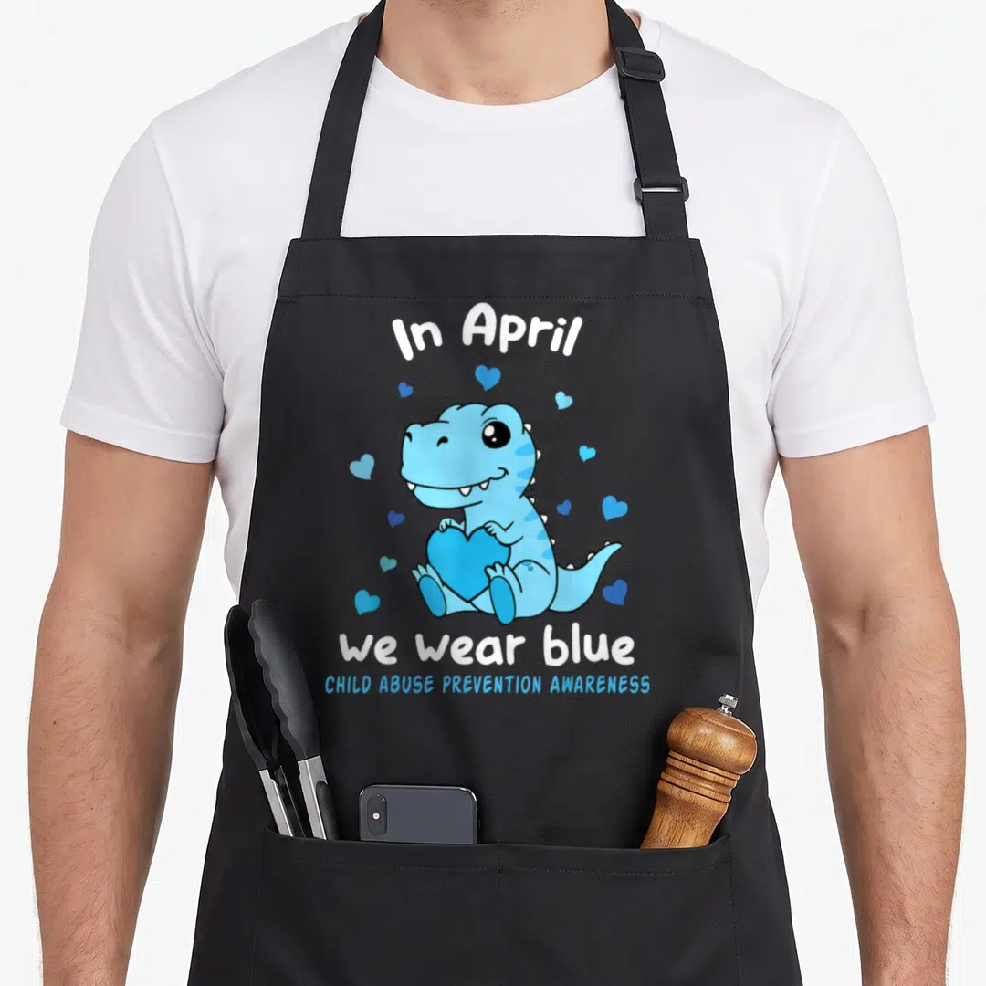 Dino blue april apron - Blue cartoon dinosaur holding heart surrounded by small hearts with awareness text — shown on a black cotton canvas apron against a white background