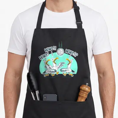 Volleyball bird apron - Three cartoon seagulls looking up at a volleyball with MINE speech bubbles — shown on a black cotton canvas apron against a white background
