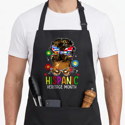 Hispanic teacher apron - Cartoon woman with flag glasses and Hispanic Heritage Month text surrounded by smiley flowers — shown on a black cotton canvas apron against a white background
