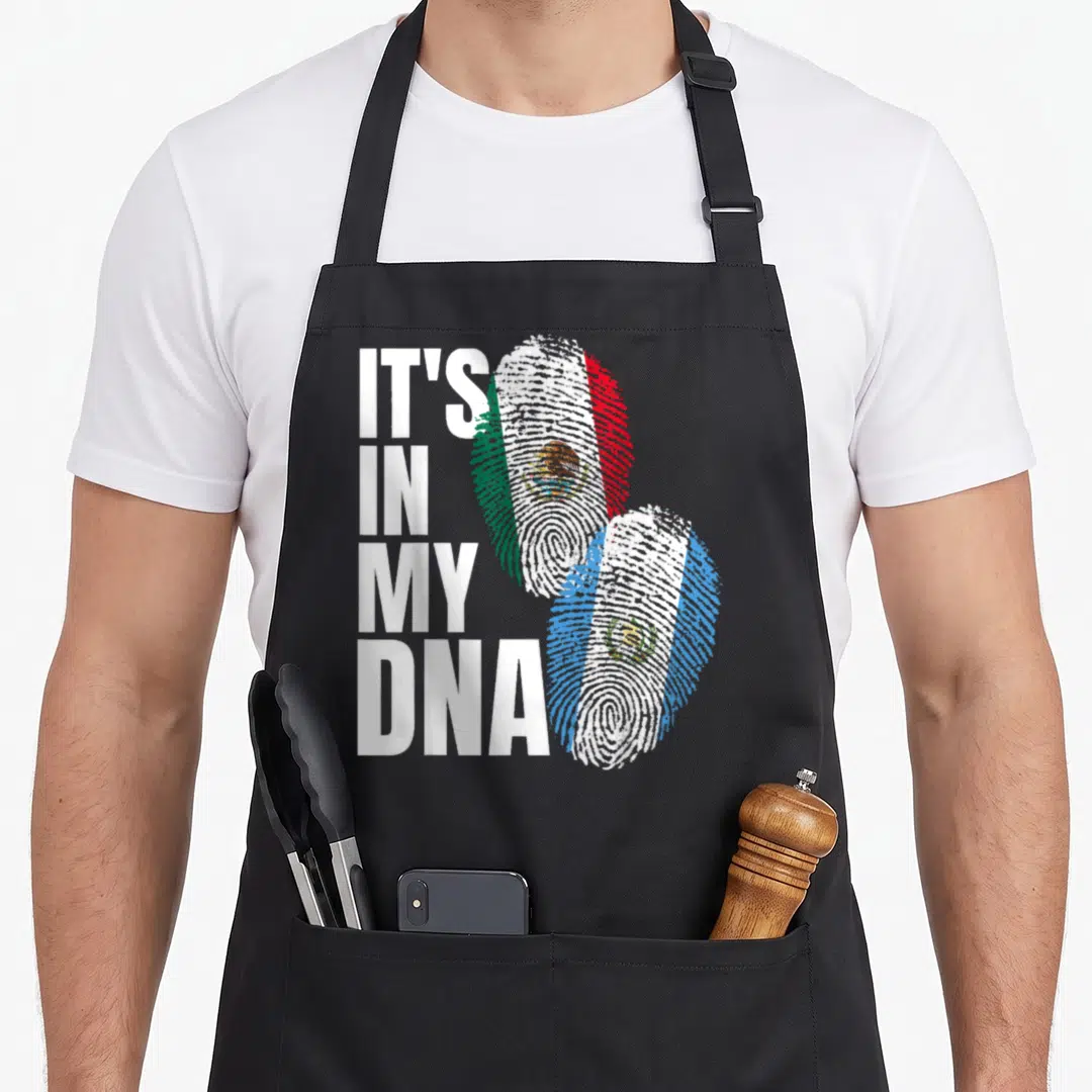 Guatemalan mexican apron - IT'S IN MY DNA text next to two fingerprints filled with Mexican and Guatemalan flags — shown on a black cotton canvas apron against a white background