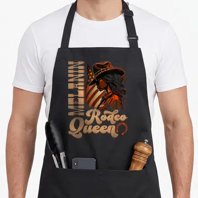 Country african american aprons - Woman in cowboy hat with vertical MELANIN text and Rodeo Queen script in orange brown — shown on a black cotton canvas apron against a white background