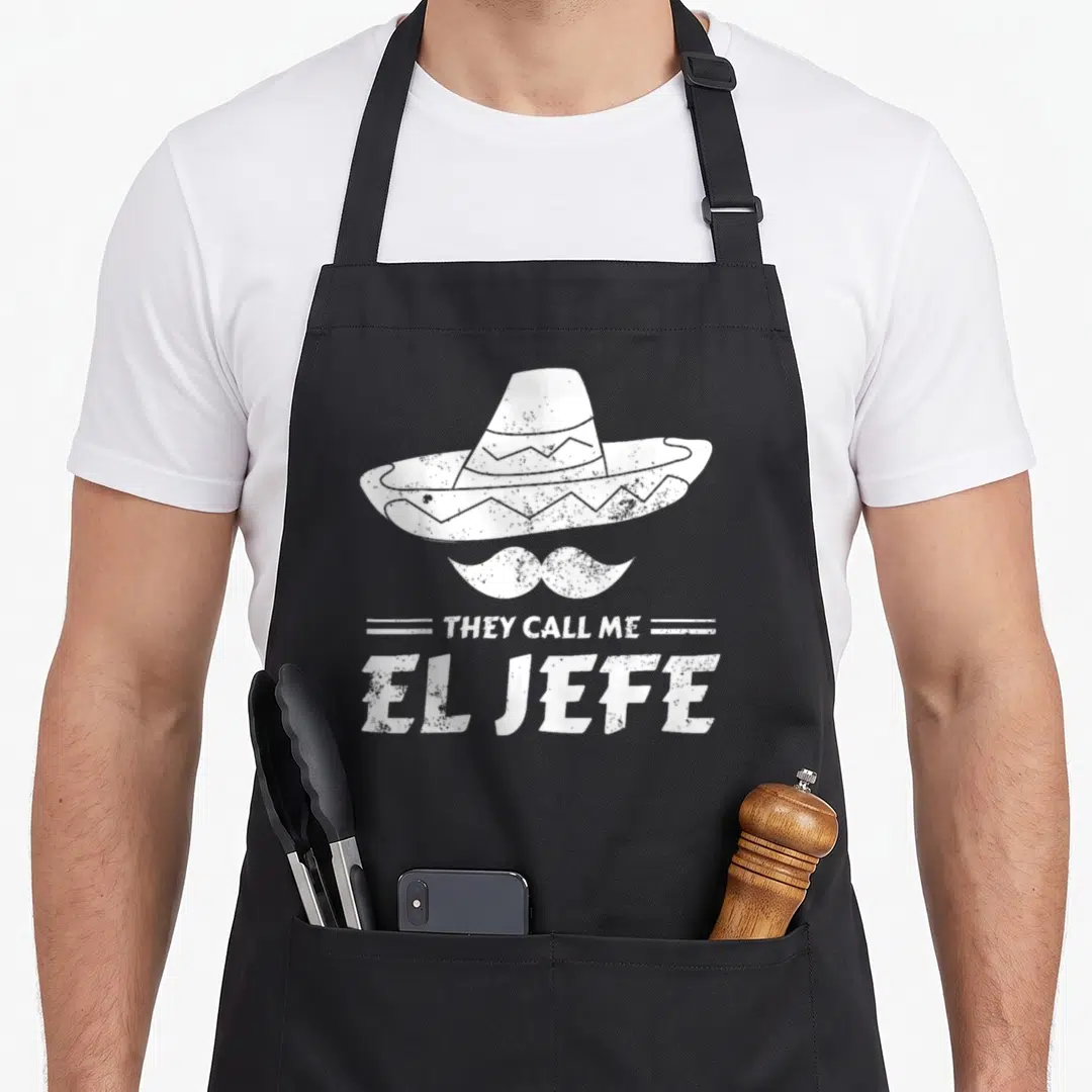 Mexican boss apron - White distressed sombrero and mustache above stacked text they call me el jefe — shown on a black cotton canvas apron against a white background