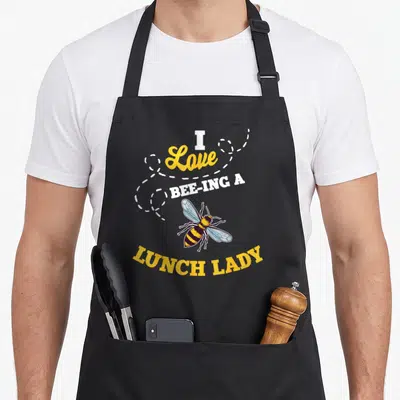 Bee lunch lady apron - Stacked text I Love Bee-ing A Lunch Lady surrounding a cartoon bee with yellow and black stripes — shown on a black cotton canvas apron against a white background