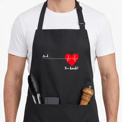 Ekg beat quotes apron - Red heart with white EKG line and text And... I'm back! — shown on a black cotton canvas apron against a white background