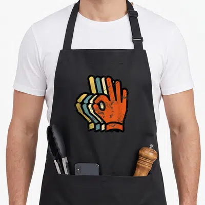 Scuba hand lover apron - Three stacked retro-style hands in OK gesture, colored orange blue yellow black — shown on a black cotton canvas apron against a white background