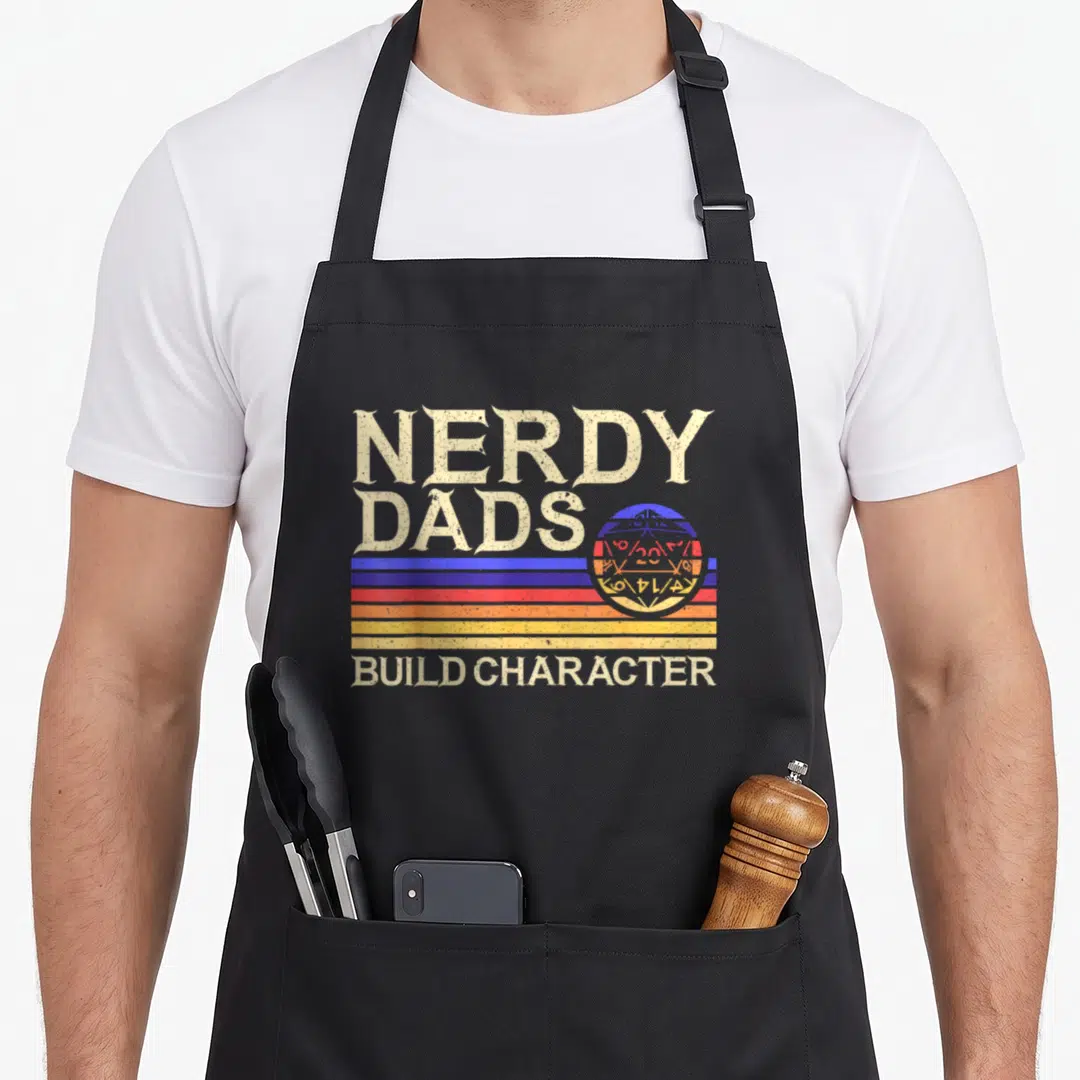 Nerdy gaming apron - Retro text NERDY DADS BUILD CHARACTER over blue red yellow orange stripes and d20 planet — shown on a black cotton canvas apron against a white background