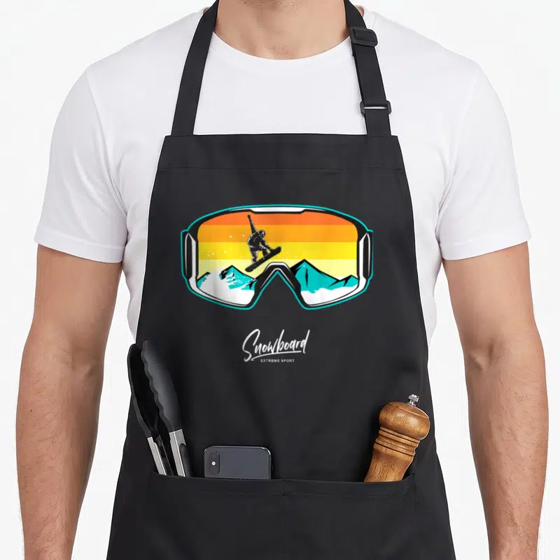 Snowboarder snowboarding player apron - Cartoon snowboarder jumping over cyan mountains inside a goggle frame — shown on a black cotton canvas apron against a white background