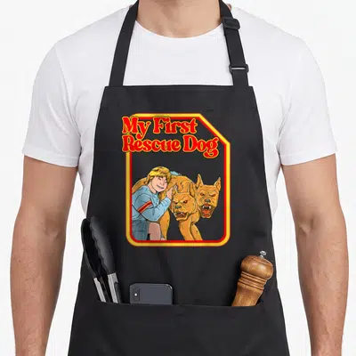 Dark grill rescue apron - Child hugging two-headed tan dog under My First Rescue Dog text in red and yellow border — shown on a black cotton canvas apron against a white background