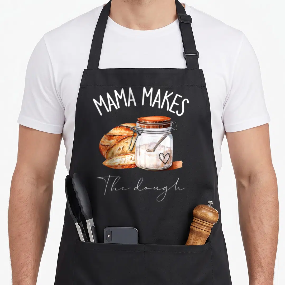 Mama homemade apron - Watercolor loaf and jar with MAMA MAKES The dough text on grey background — shown on a black cotton canvas apron against a white background