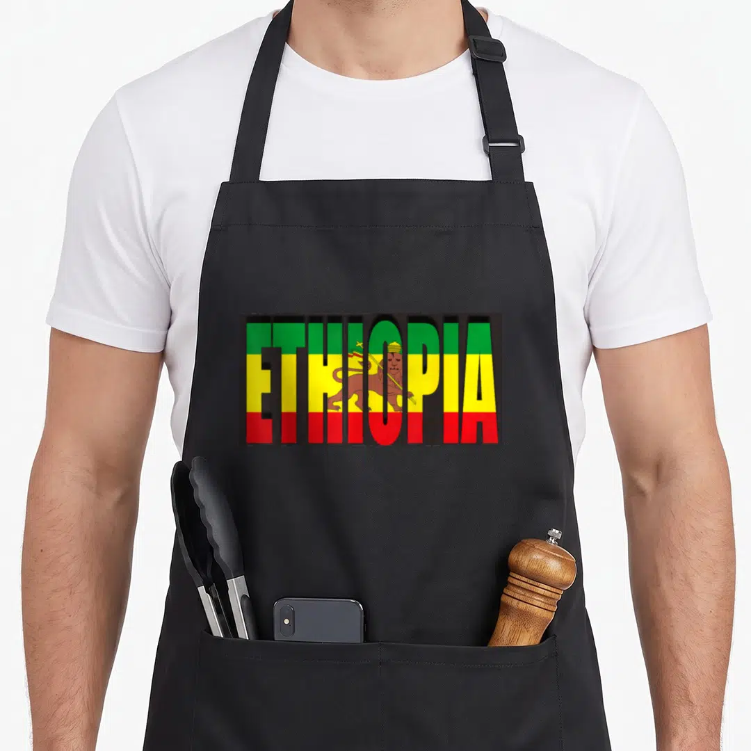 Rastafarian ethiopian apron - ETHIOPIA text filled with green yellow red stripes and central Lion of Judah icon — shown on a black cotton canvas apron against a white background