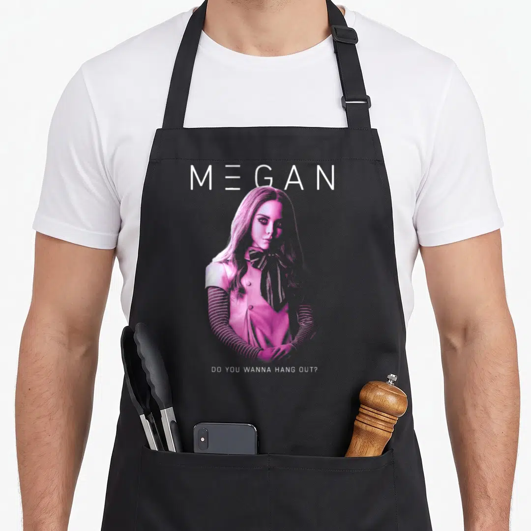 M3gan nbc apron - Pink woman illustration with MEGAN text and DO YOU WANNA HANG OUT question — shown on a black cotton canvas apron against a white background