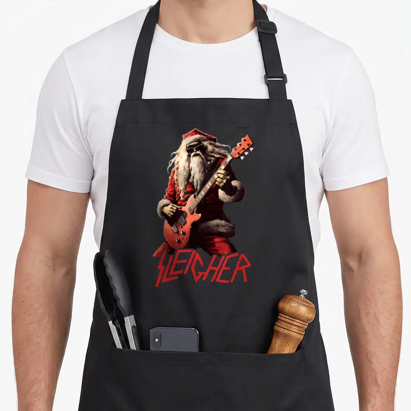 Christmas heavy metal apron - Realistic Santa playing red guitar with Sleighher text in heavy metal font — shown on a black cotton canvas apron against a white background