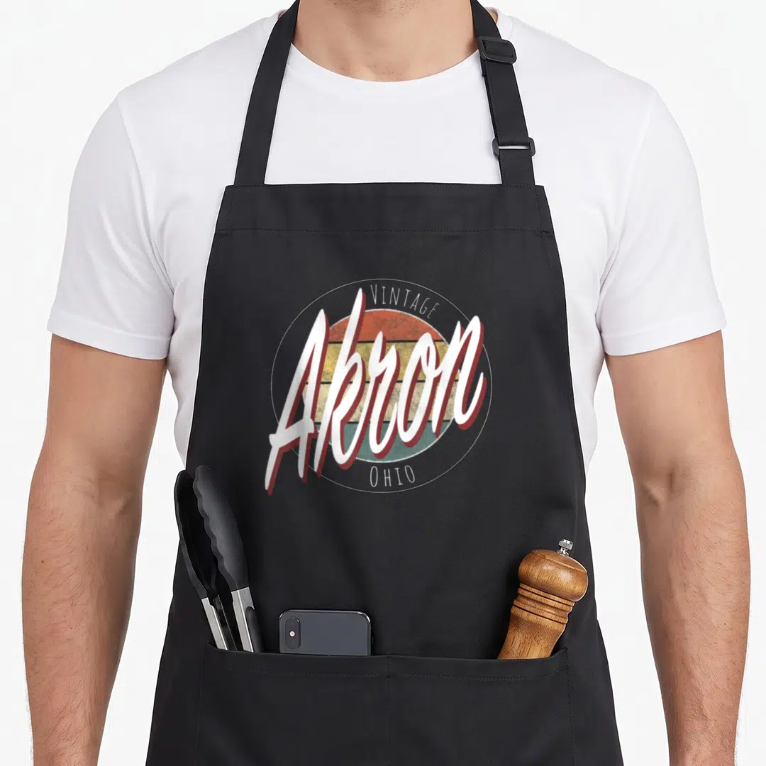 Cute ohio akron apron - Retro VINTAGE Akron OHIO text over striped orange yellow teal sun on black apron — shown on a black cotton canvas apron against a white background