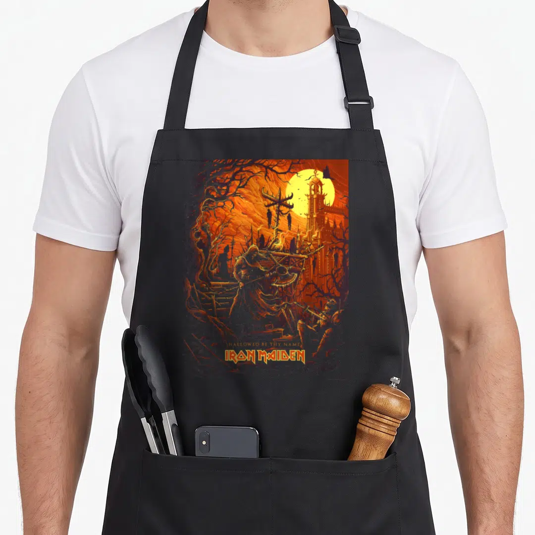 Number camping apron - Iron Maiden Eddie axe scene with Hallowed Be Thy Name text in orange and grey — shown on a black cotton canvas apron against a white background