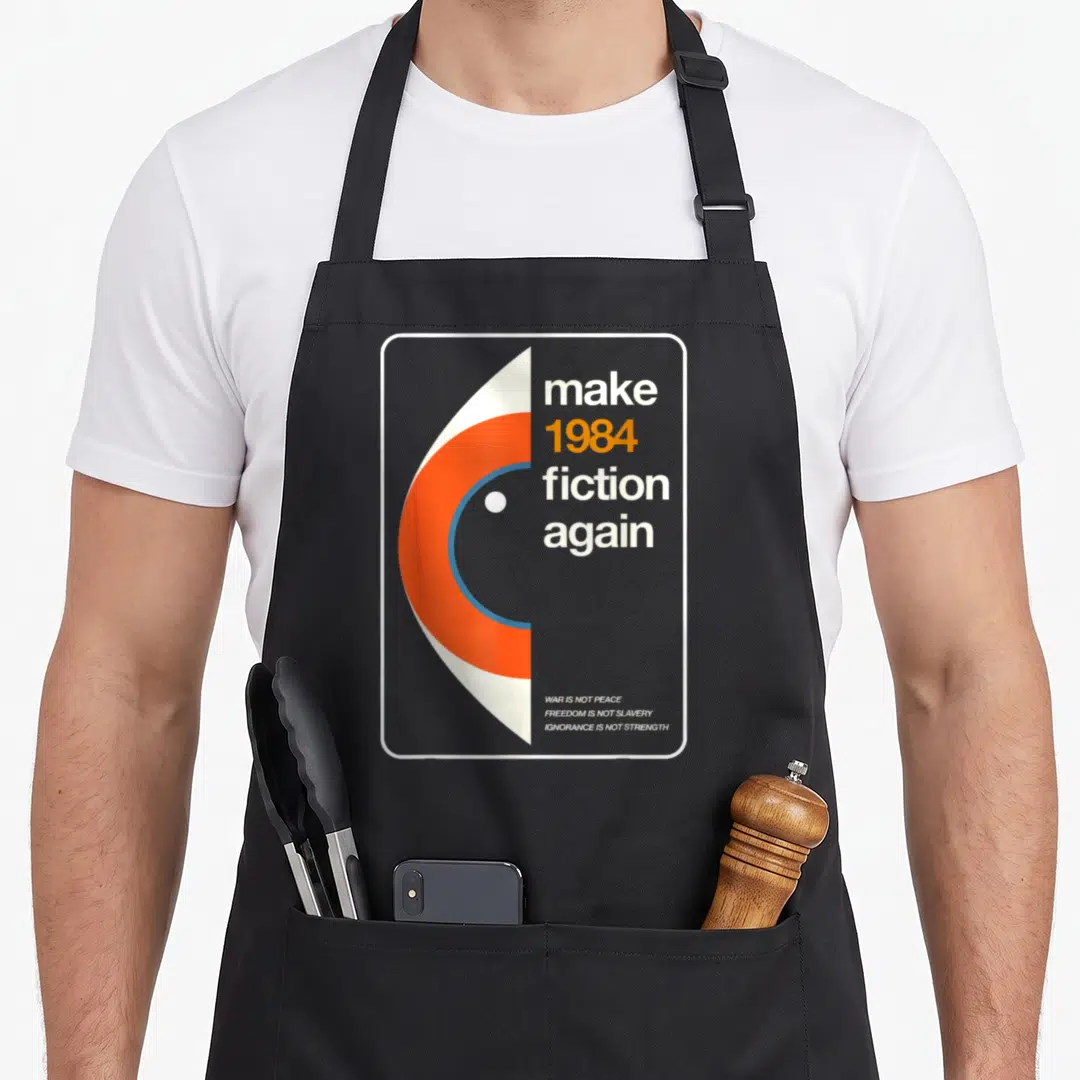 Freedom fiction apron - Abstract eye graphic next to make 1984 fiction again text in white orange and blue — shown on a black cotton canvas apron against a white background
