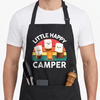 Toddler camping apron - Three smiling marshmallows on stumps around a campfire under LITTLE HAPPY CAMPER text — shown on a black cotton canvas apron against a white background