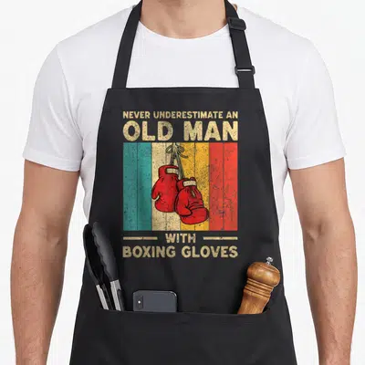 Underestimate gloves and apron - Red boxing gloves hanging by laces over vertical teal, white, yellow, and red stripes — shown on a black cotton canvas apron against a white background