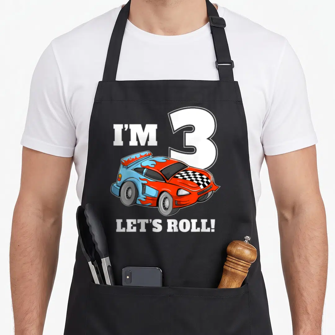 Toddler car apron - Cartoon race car with I'M 3 LET'S ROLL text in blue red orange — shown on a black cotton canvas apron against a white background