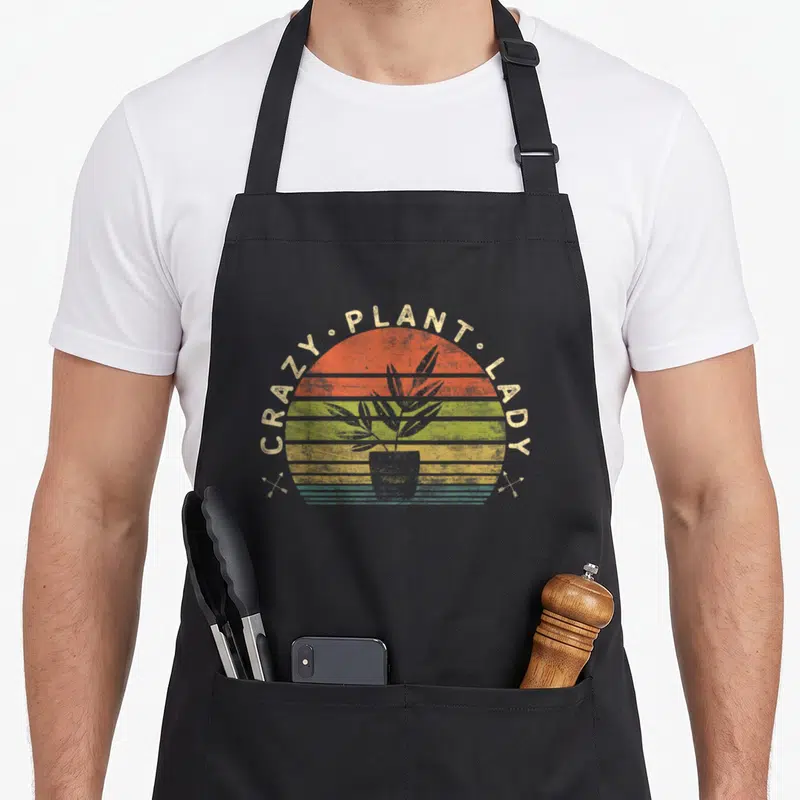 Gardener plant lady apron - Retro striped sun with potted plant and arched text CRAZY PLANT LADY — shown on a black cotton canvas apron against a white background