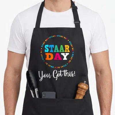 Staar test kitchen apron - STAAR DAY text in colored block letters surrounded by hearts with You Got this! script below — shown on a black cotton canvas apron against a white background
